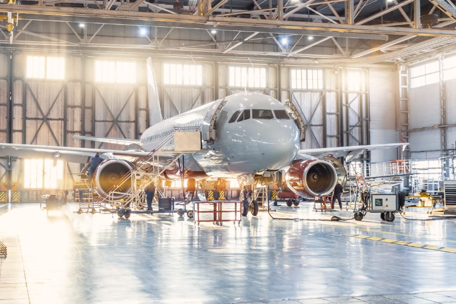 A large airplane in an airport hangar with people around.
