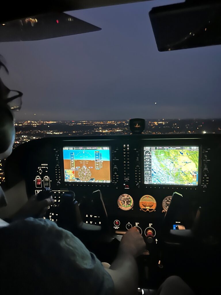 Pilot flying aircraft at night, illuminated cockpit.
