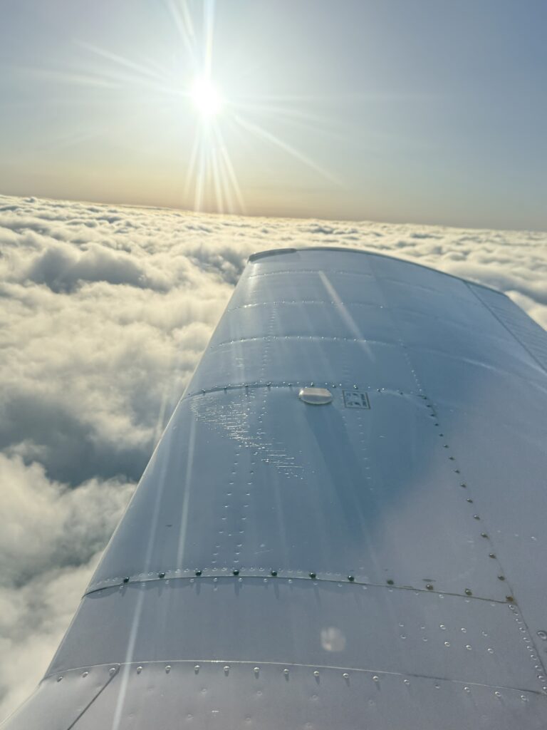 Sunlit airplane wing above fluffy clouds.